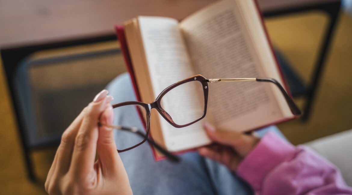woman sit on sofa read book and hold eyeglasses